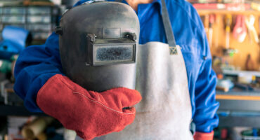 A man welder with safety helmet working with arc welding machine in the workshop. Male hands in gloves for fix a piece of iron